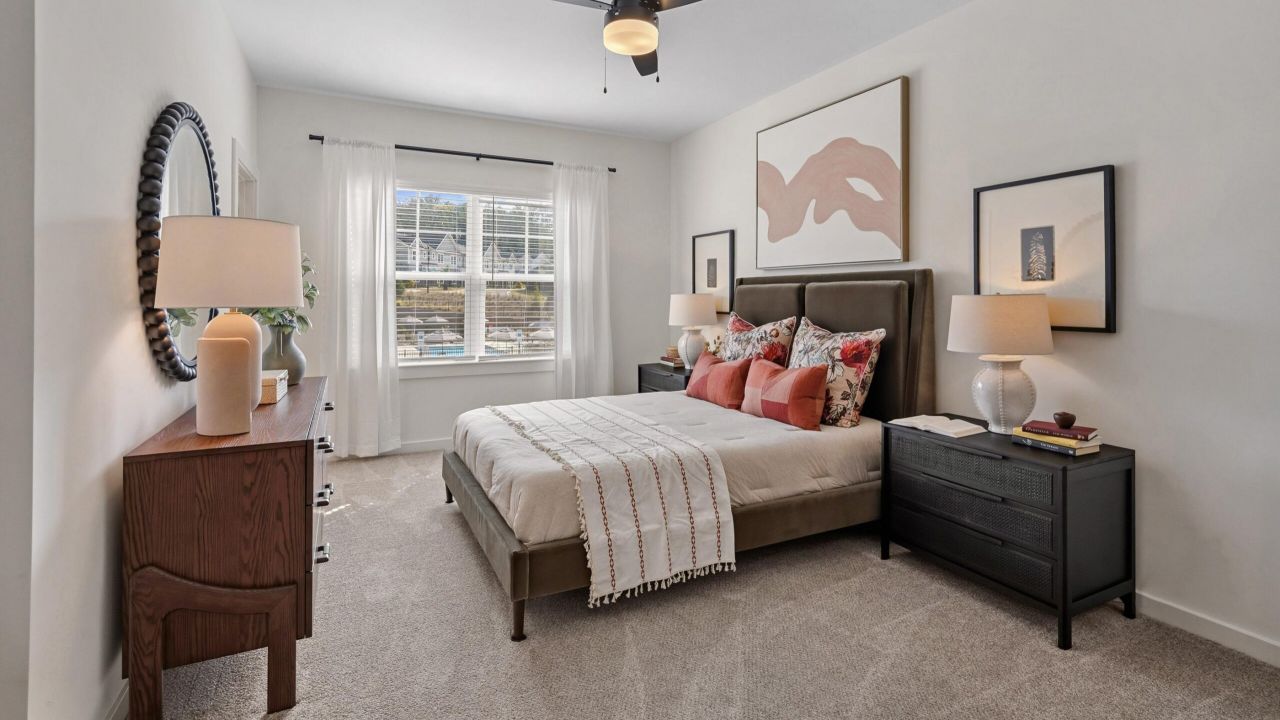 Bright bedroom with large window, double bed, neutral decor, nightstands, lamps, and abstract wall art.