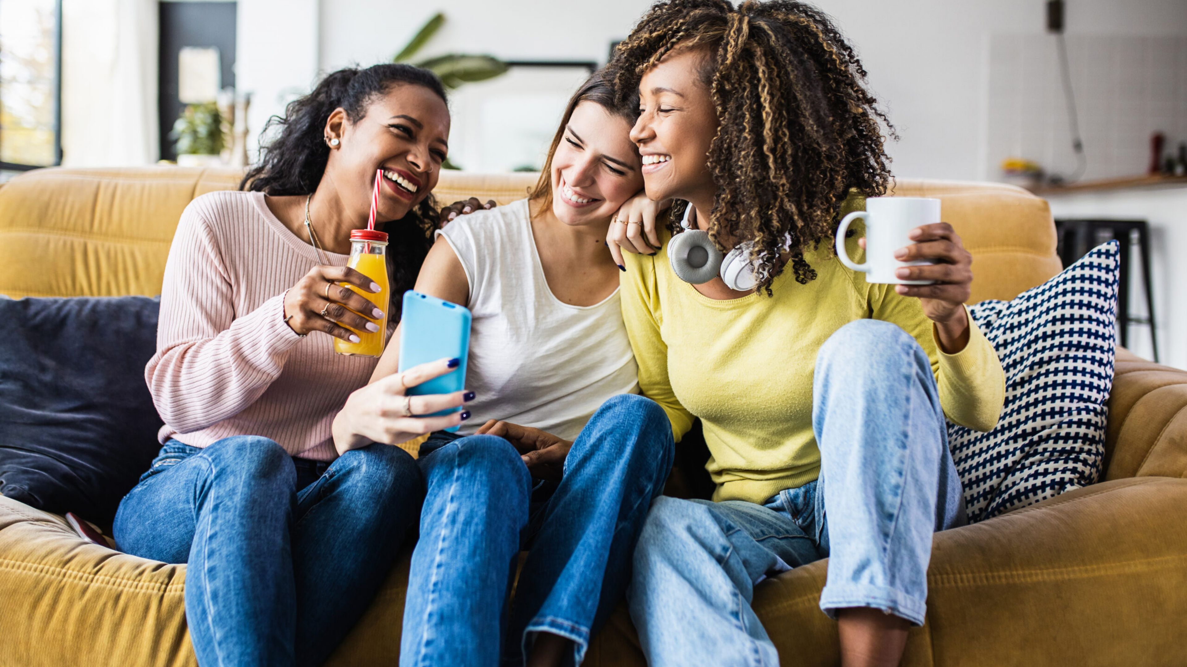 Cheerful multiracial female friends enjoying free time together at home - Three happy young adult women hanging out while - Friendship and social gathering concept