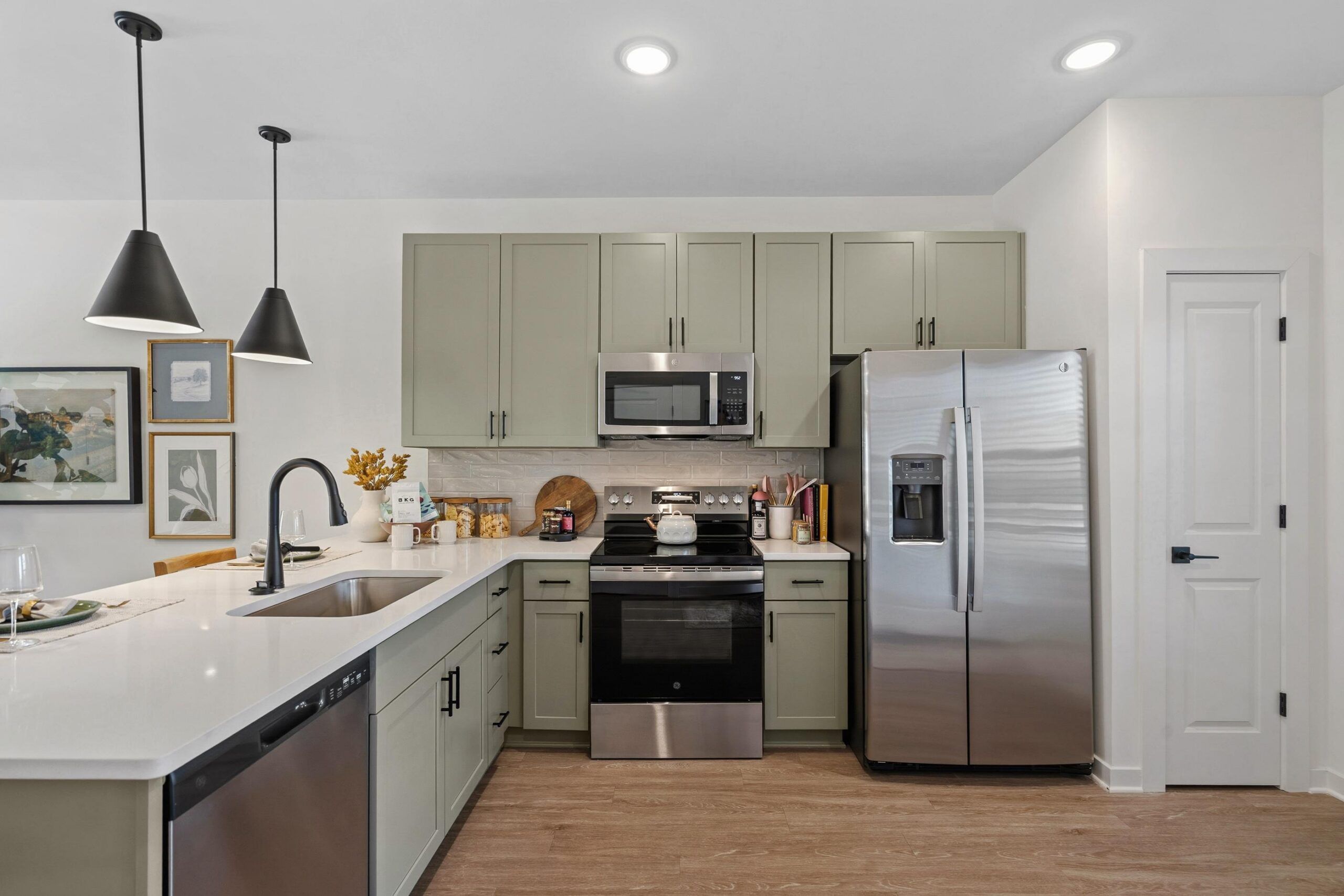 Modern kitchen with light green cabinets, stainless steel appliances, and wood flooring.